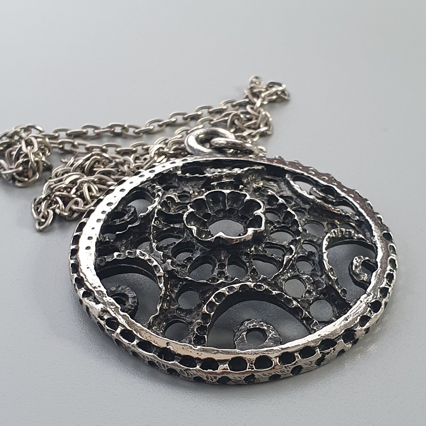 Ornate silver pendant with intricate filigree design on a chain necklace.