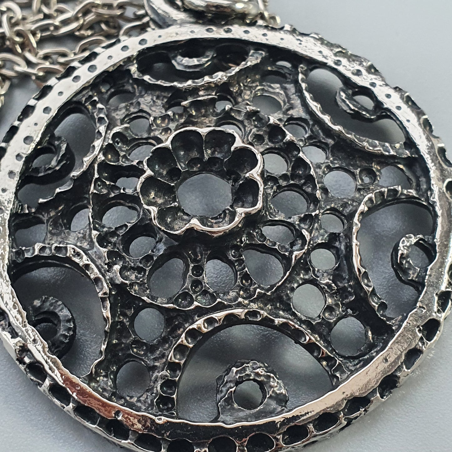 Ornate silver pendant with intricate floral and swirl cutout designs.