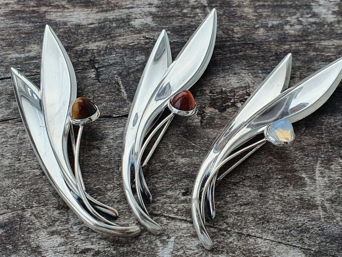 Silver brooches shaped like stylized leaves or flowers, each adorned with a single gemstone.