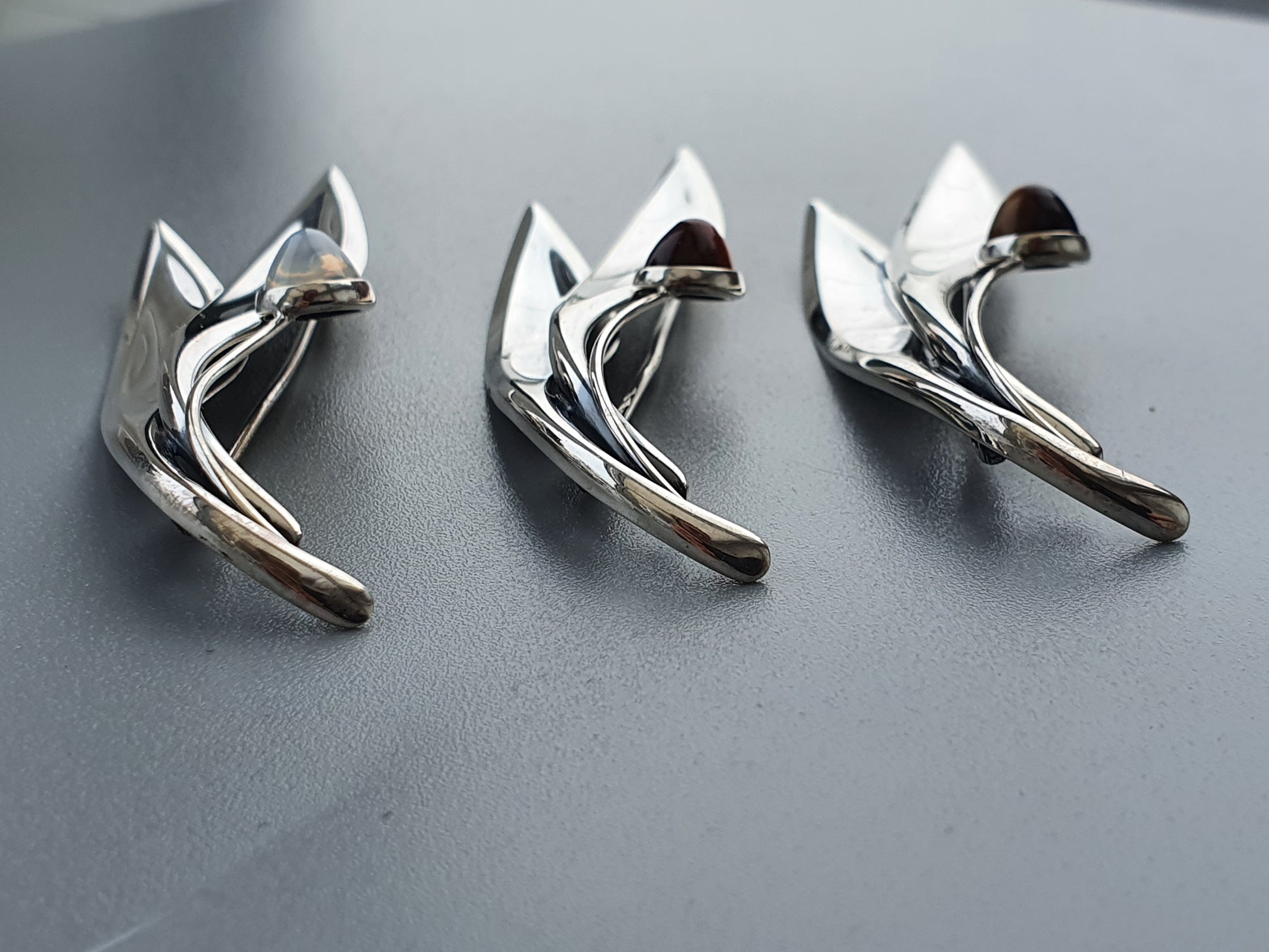 Three silver-colored metal clips or fasteners shaped like stylized cats.