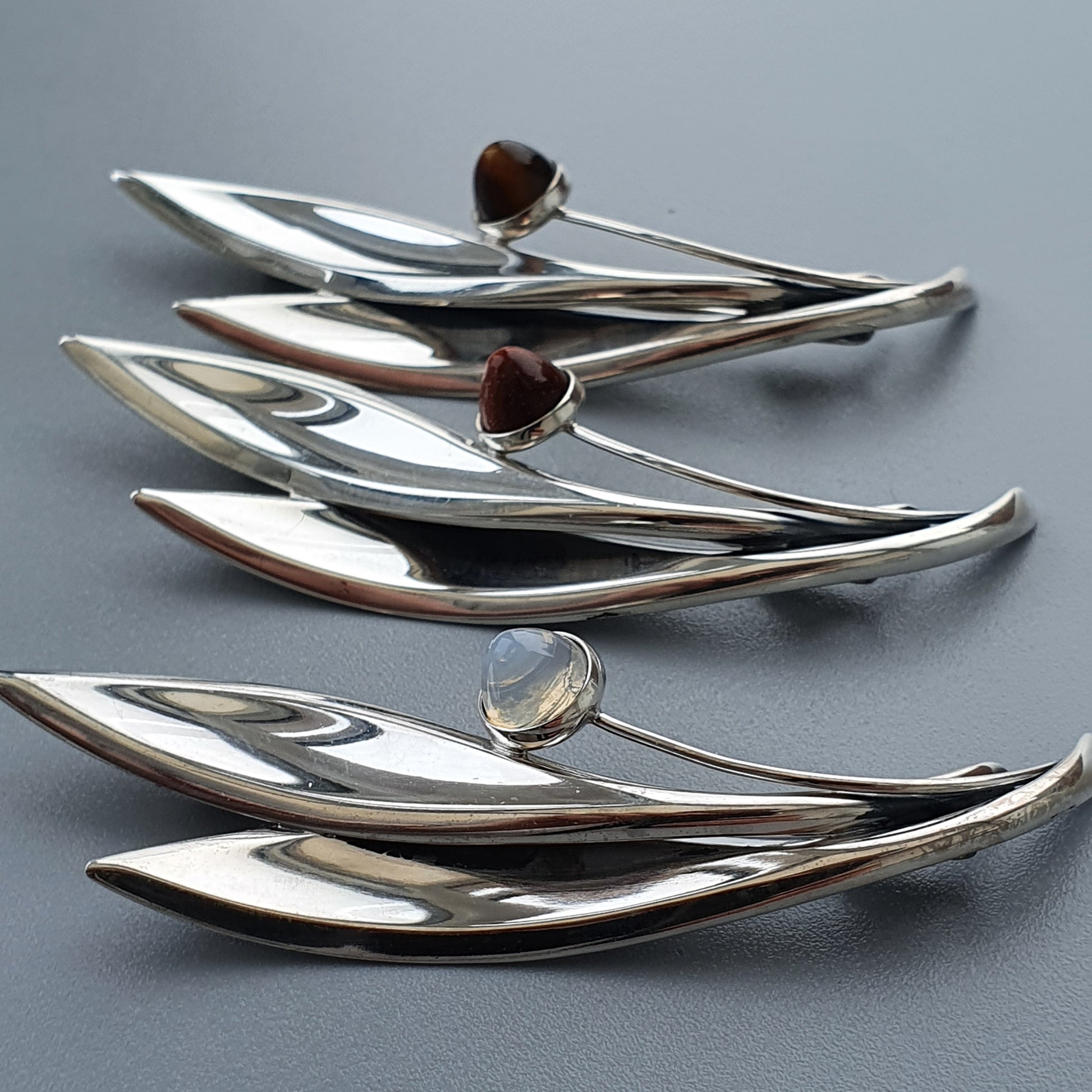 Sleek silver brooches or pins with gemstone accents in leaf-like designs.