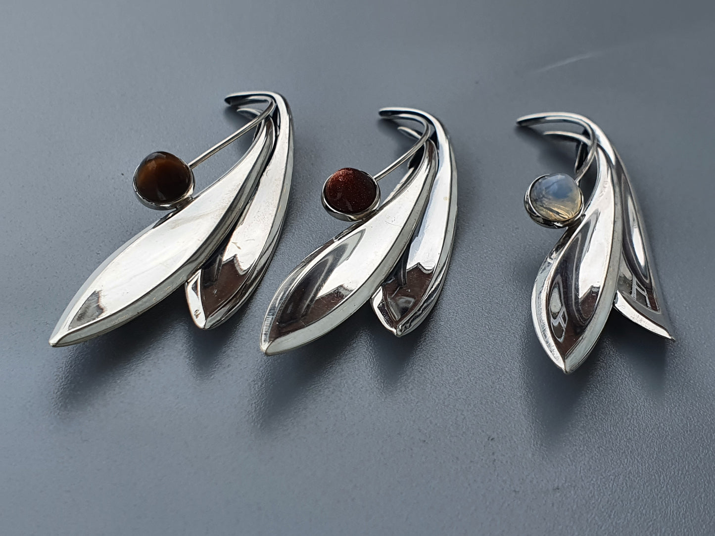 Silver leaf-shaped brooches or pendants with colored gemstones.