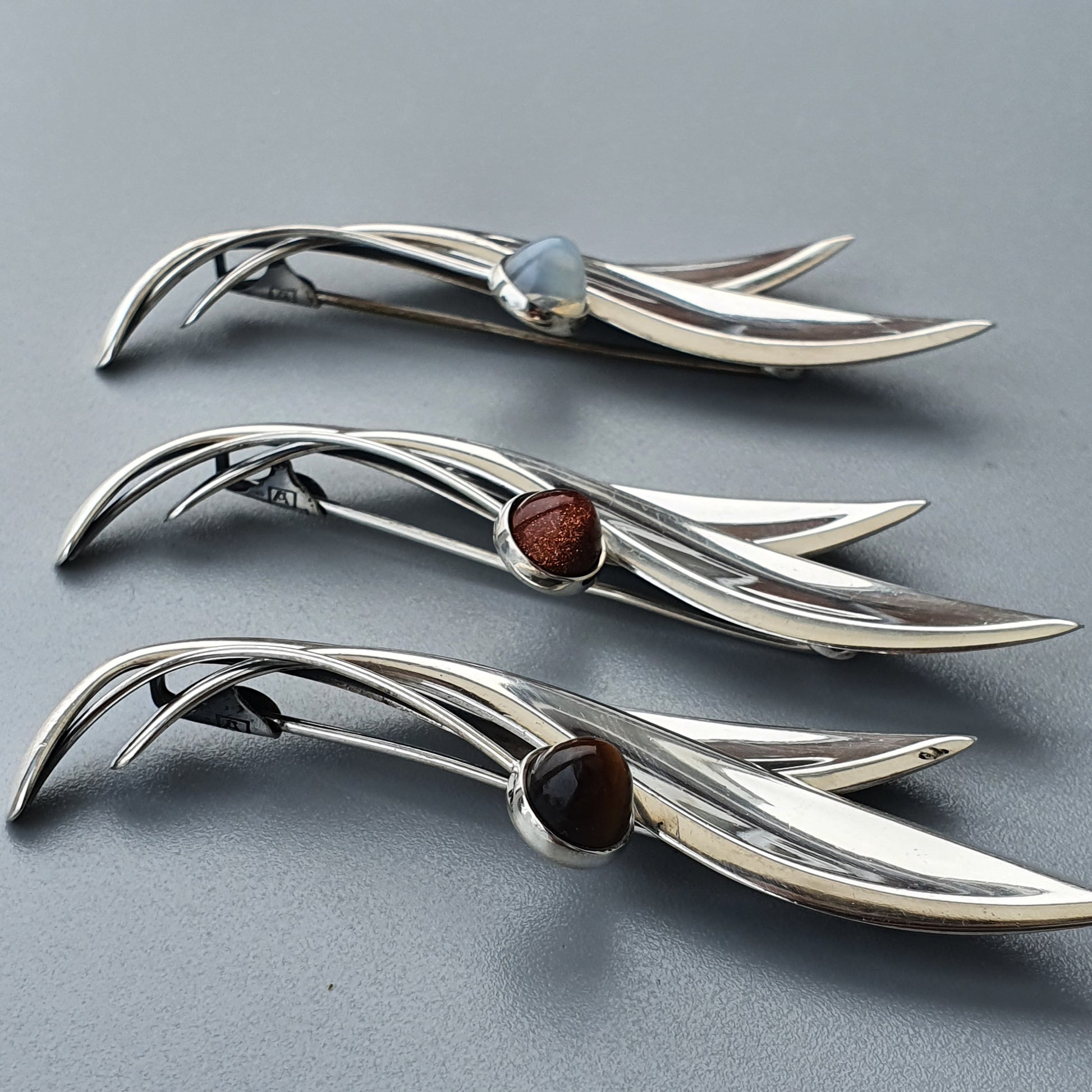 Sleek silver brooches with curved designs and inset gemstones.