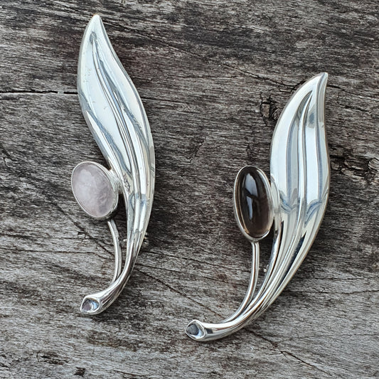 Pair of silver leaf-shaped brooches with oval gemstones.