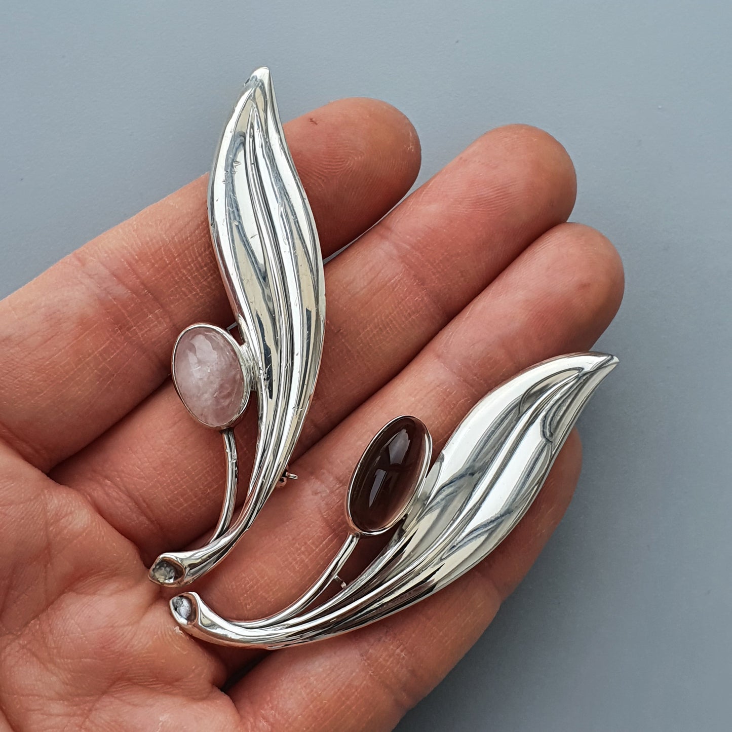 Silver leaf-shaped brooches or pendants with gemstone accents.