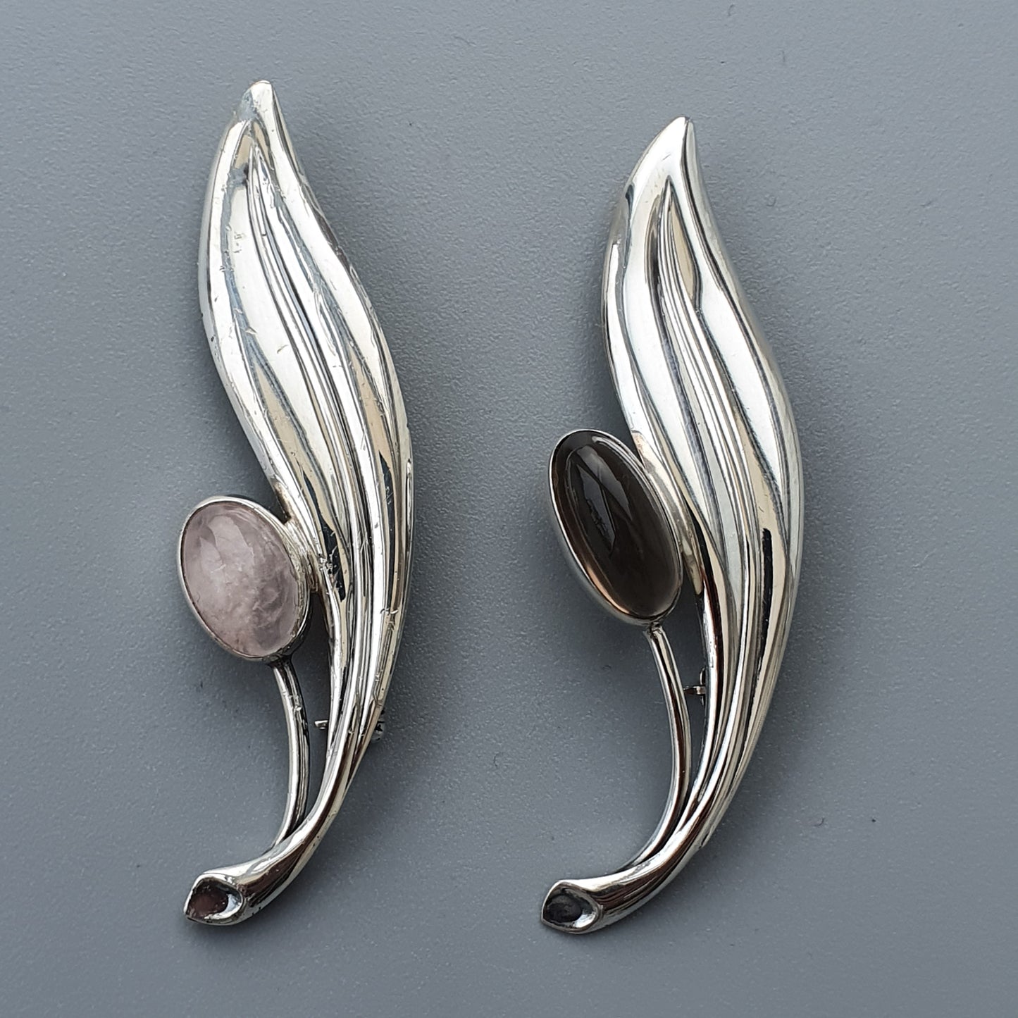 Pair of silver-toned leaf-shaped brooches with oval gemstones.