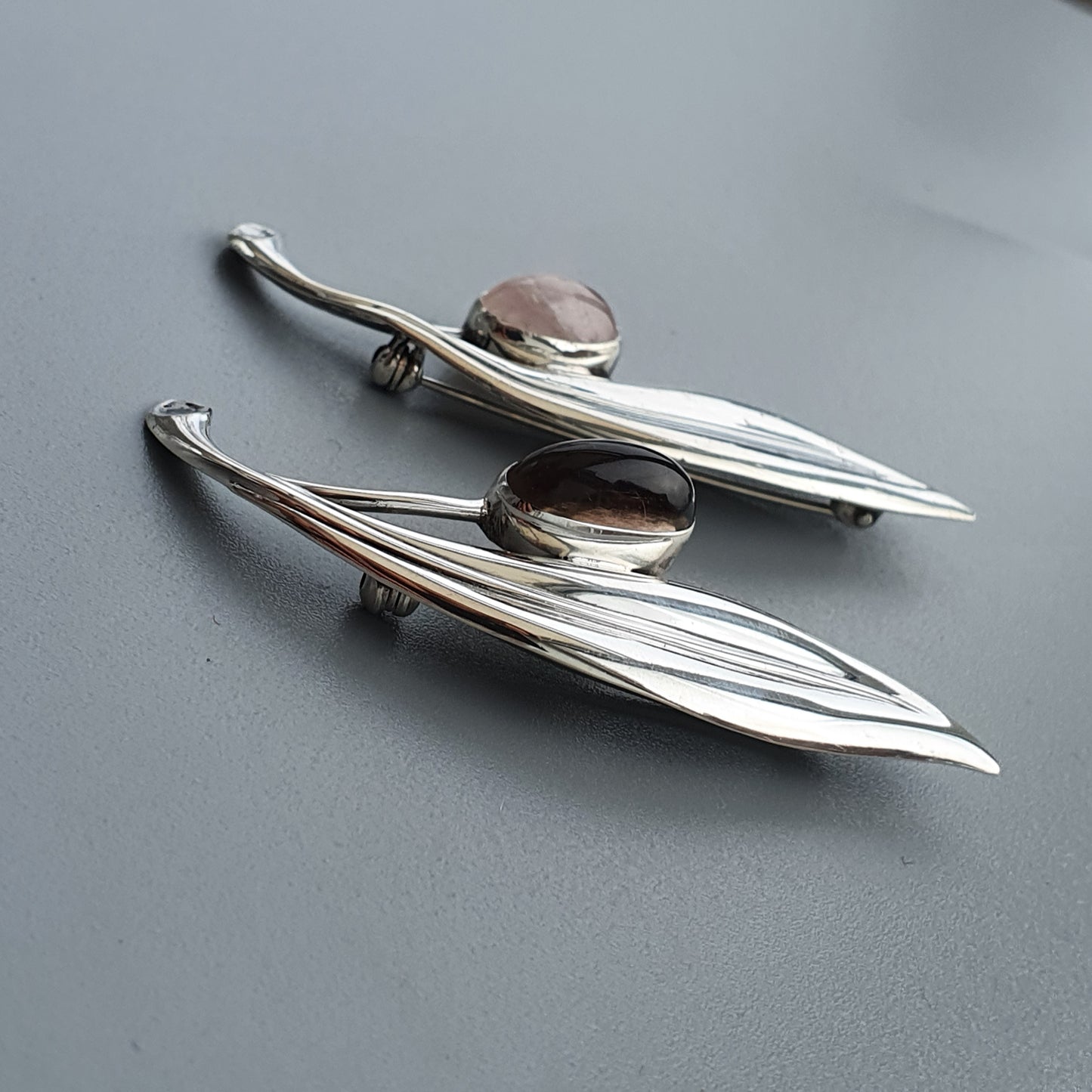 Pair of sleek, elongated silver brooches with gemstone accents.