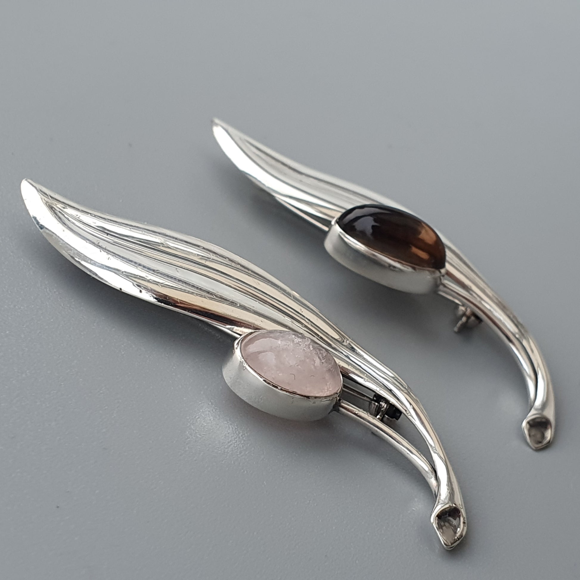 Two silver wing-shaped brooches or pins with gemstones set in the center.