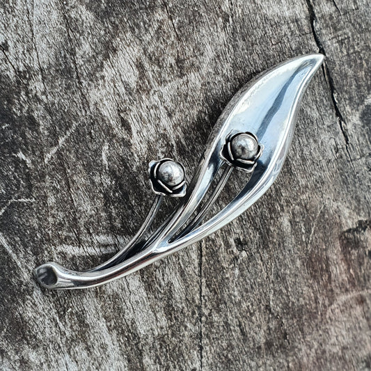 Sleek silver brooch or pin shaped like a stylized leaf with two small spheres.