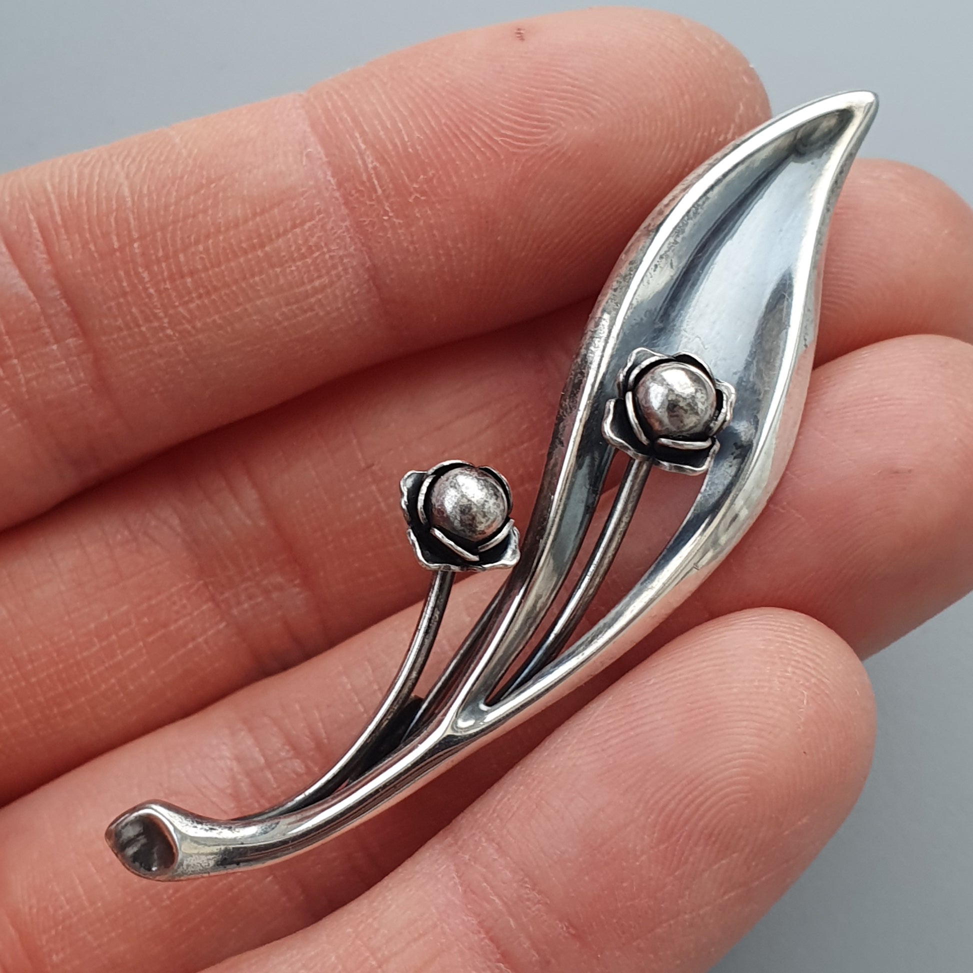 Silver leaf-shaped brooch with two small spherical accents.