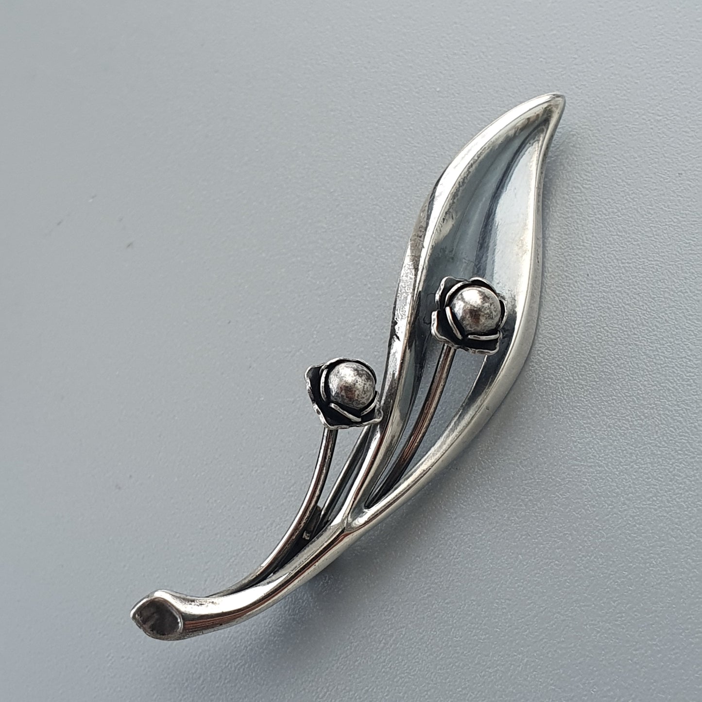 Sleek silver brooch with a curved leaf-like shape and two spherical accents.