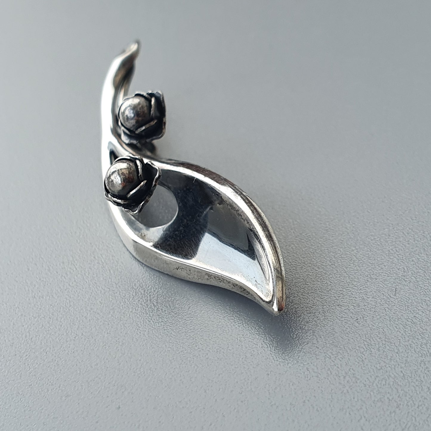 Silver pendant or brooch shaped like a stylized leaf with two small bud-like elements.