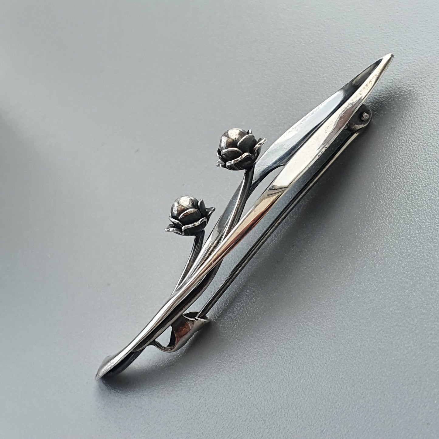 Sleek chrome car hood ornament with two stylized floral elements.