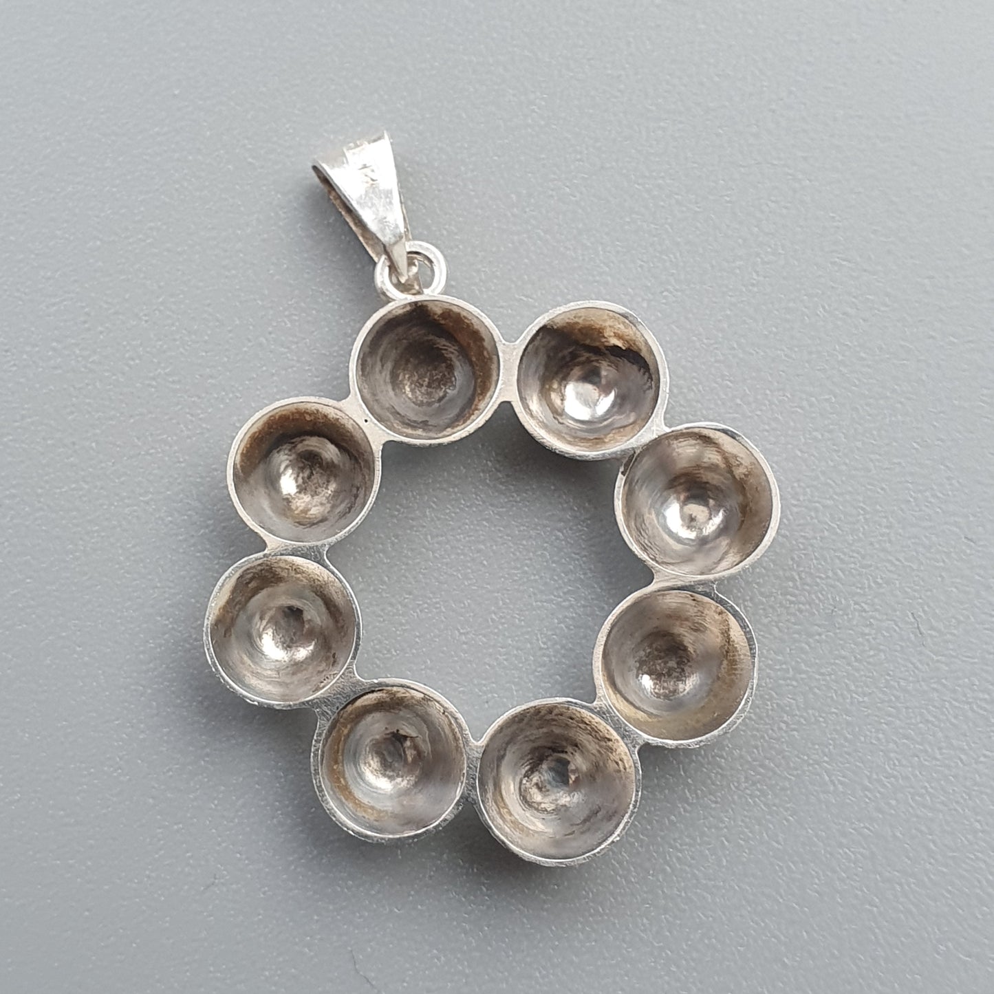 Silver pendant featuring a circular design made of eight small cup-like shapes.