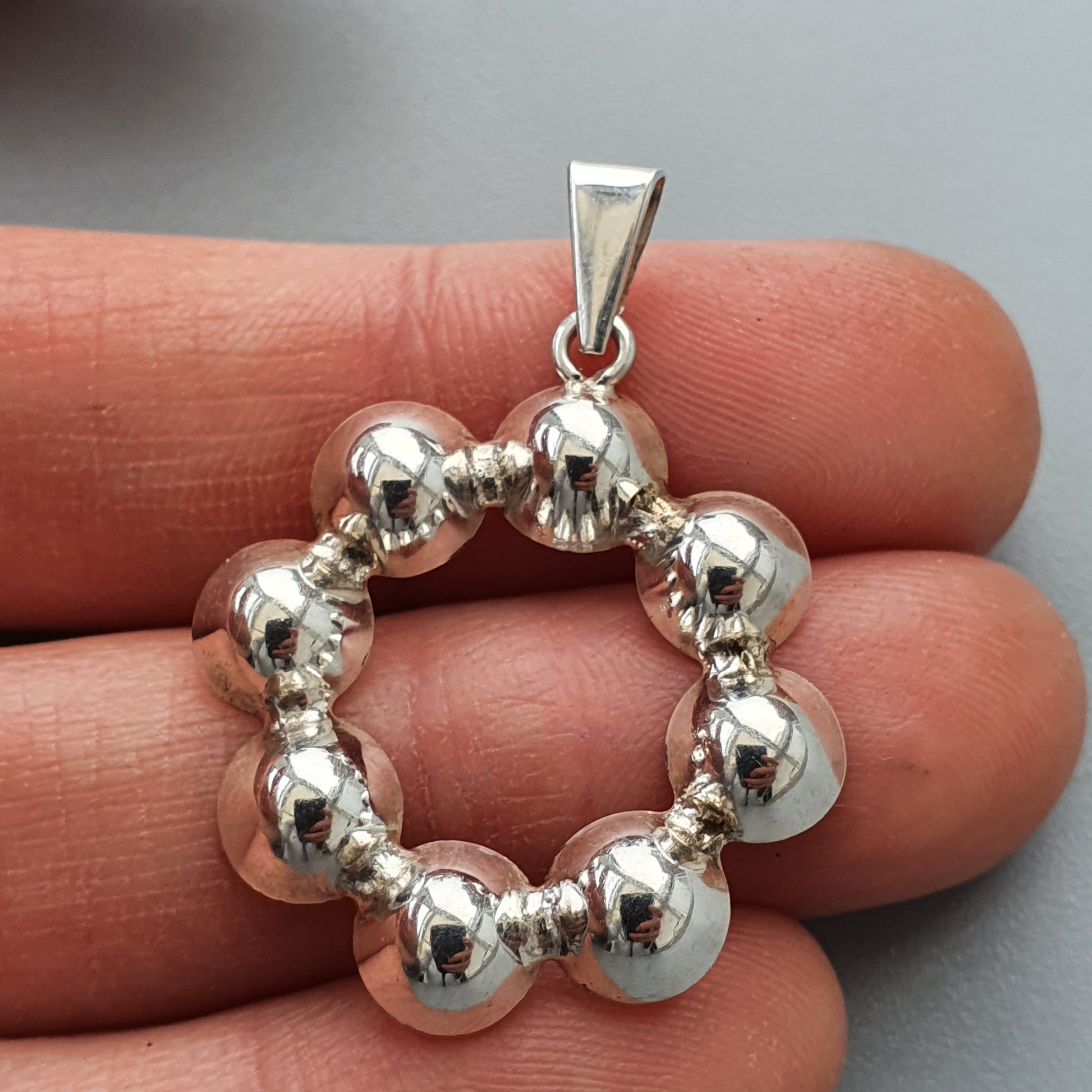 Silver pendant featuring a circular design of alternating larger and smaller spheres.