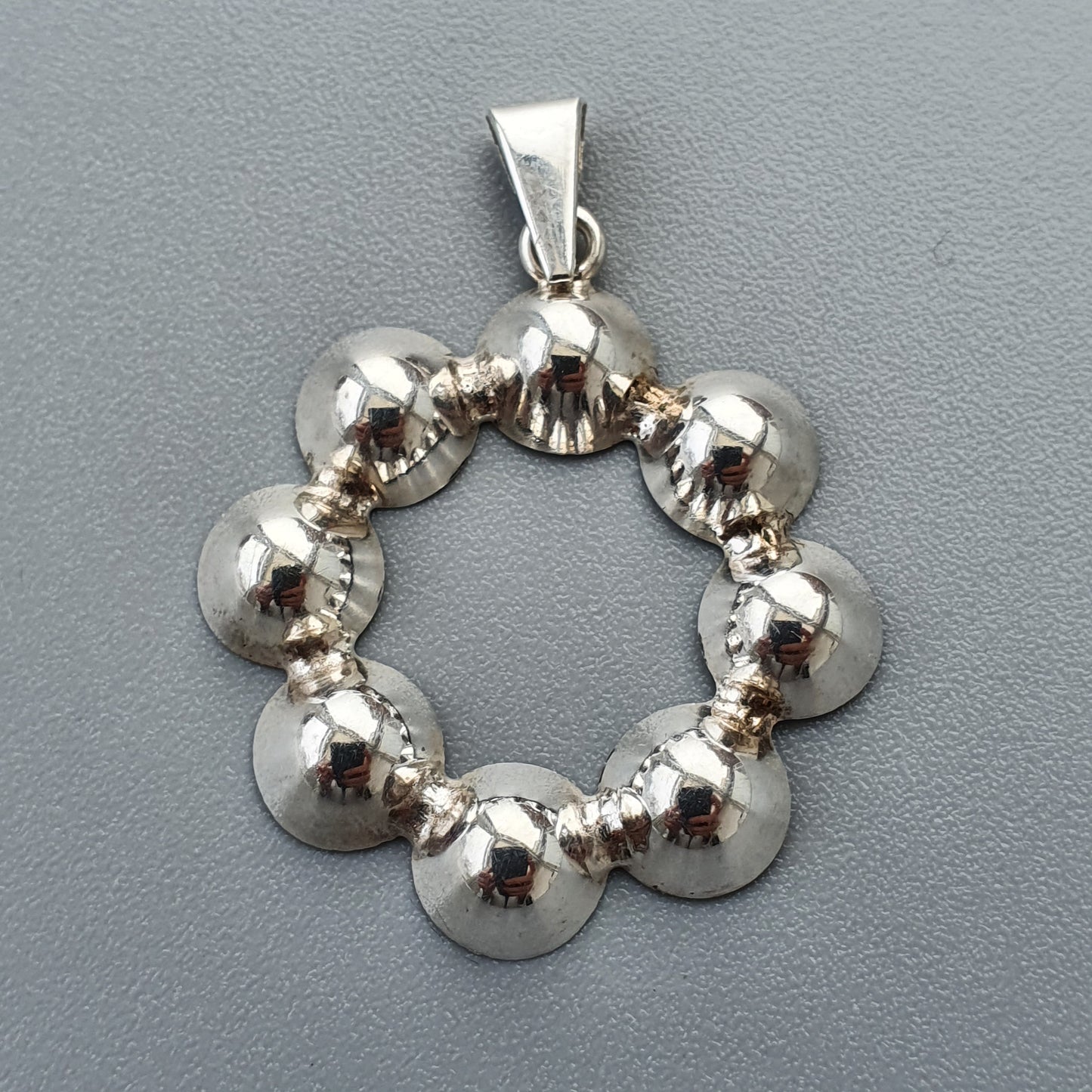 Silver pendant featuring a circular design of connected spherical beads.