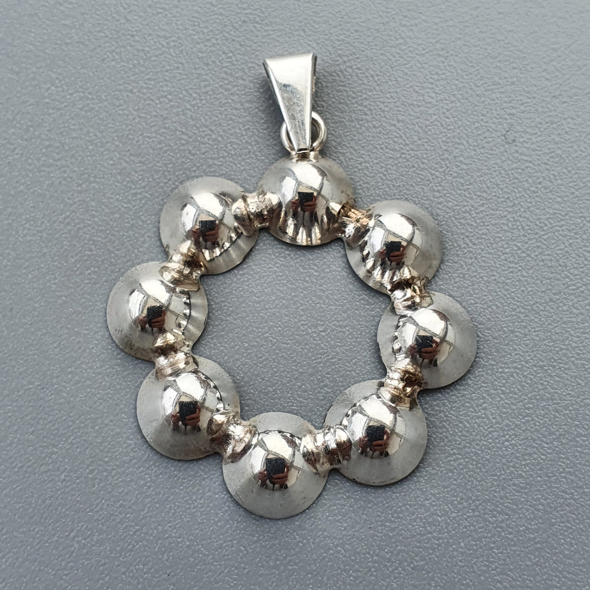 Silver pendant featuring a circular design of connected spherical beads.