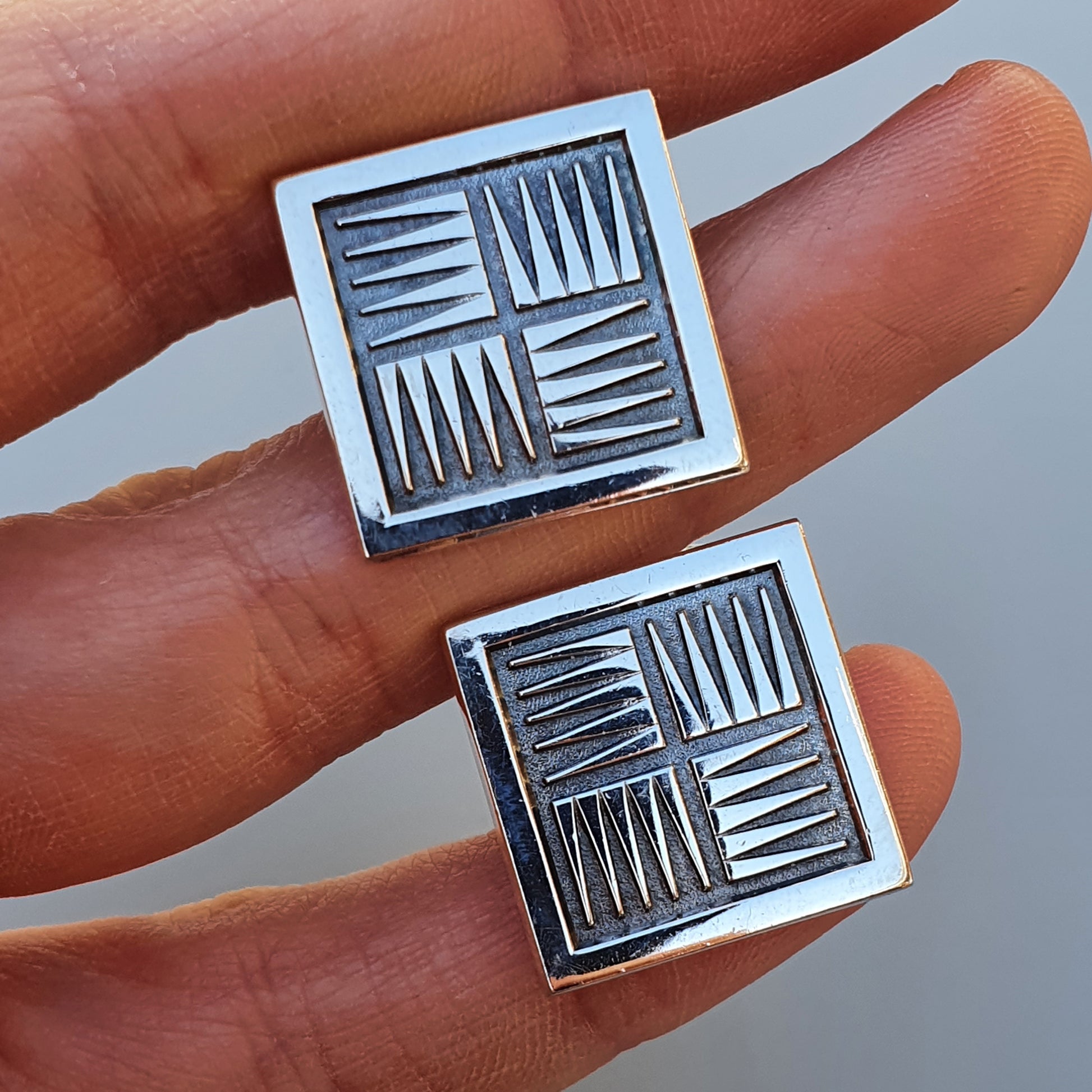 Square metal cufflinks with a geometric pattern of lines in four quadrants.