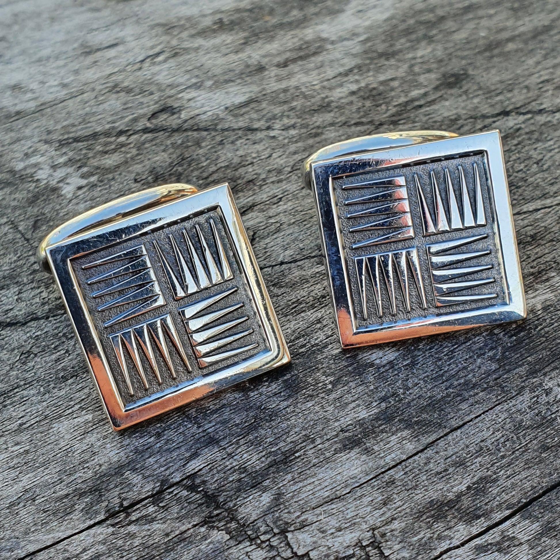 Pair of square silver cufflinks with geometric line patterns.