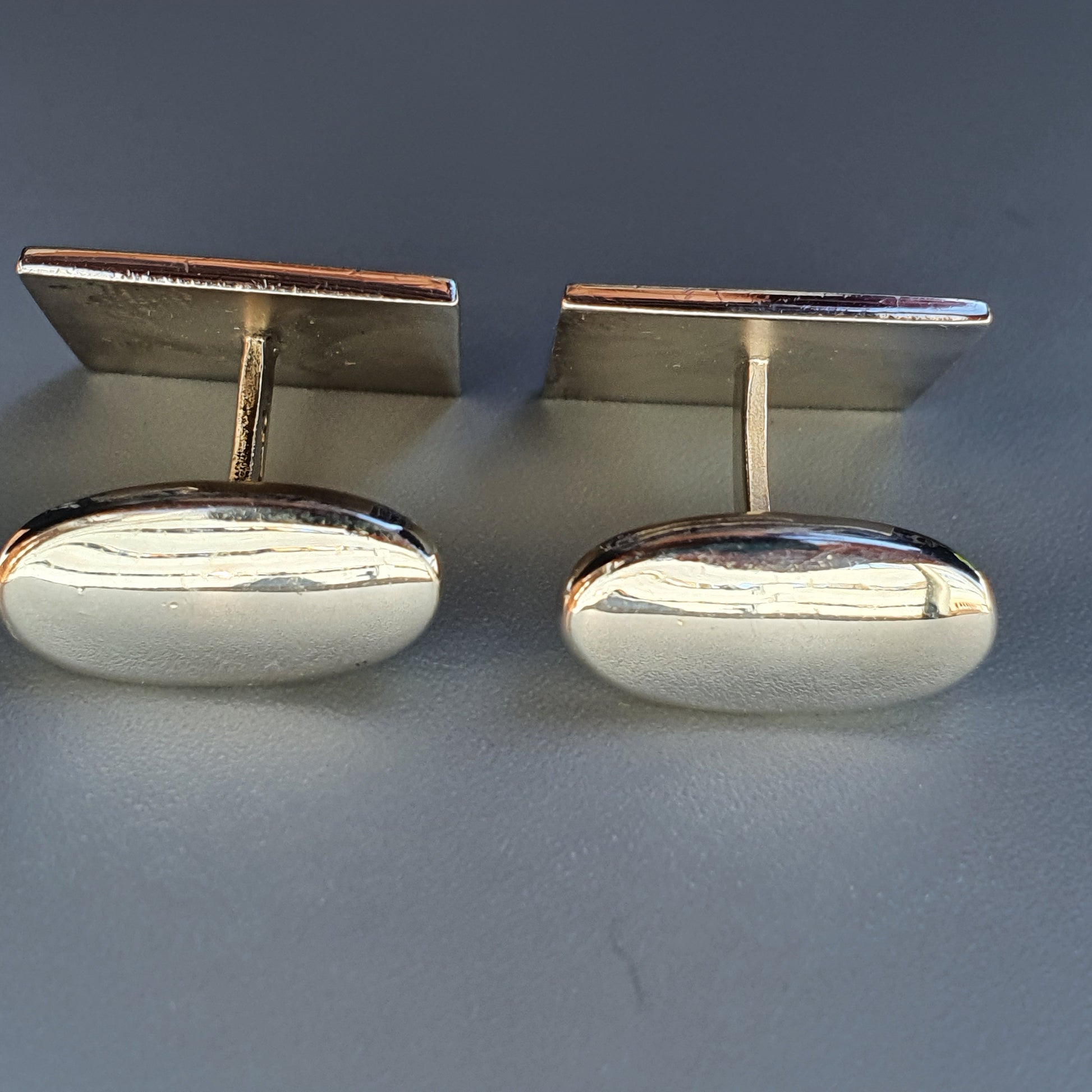 Pair of oval silver cufflinks with rectangular tops.