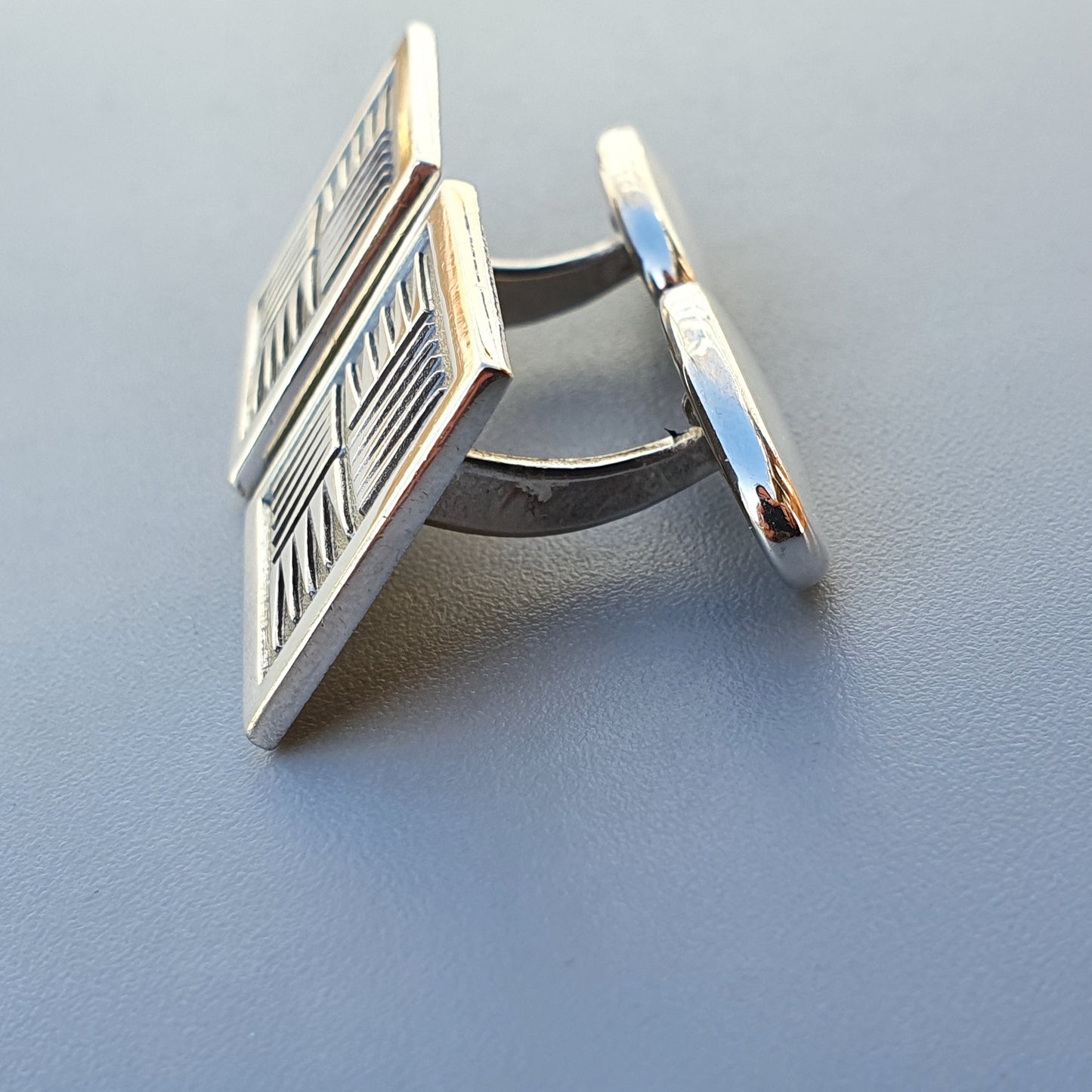 Silver cufflink with a geometric pattern on its square face.