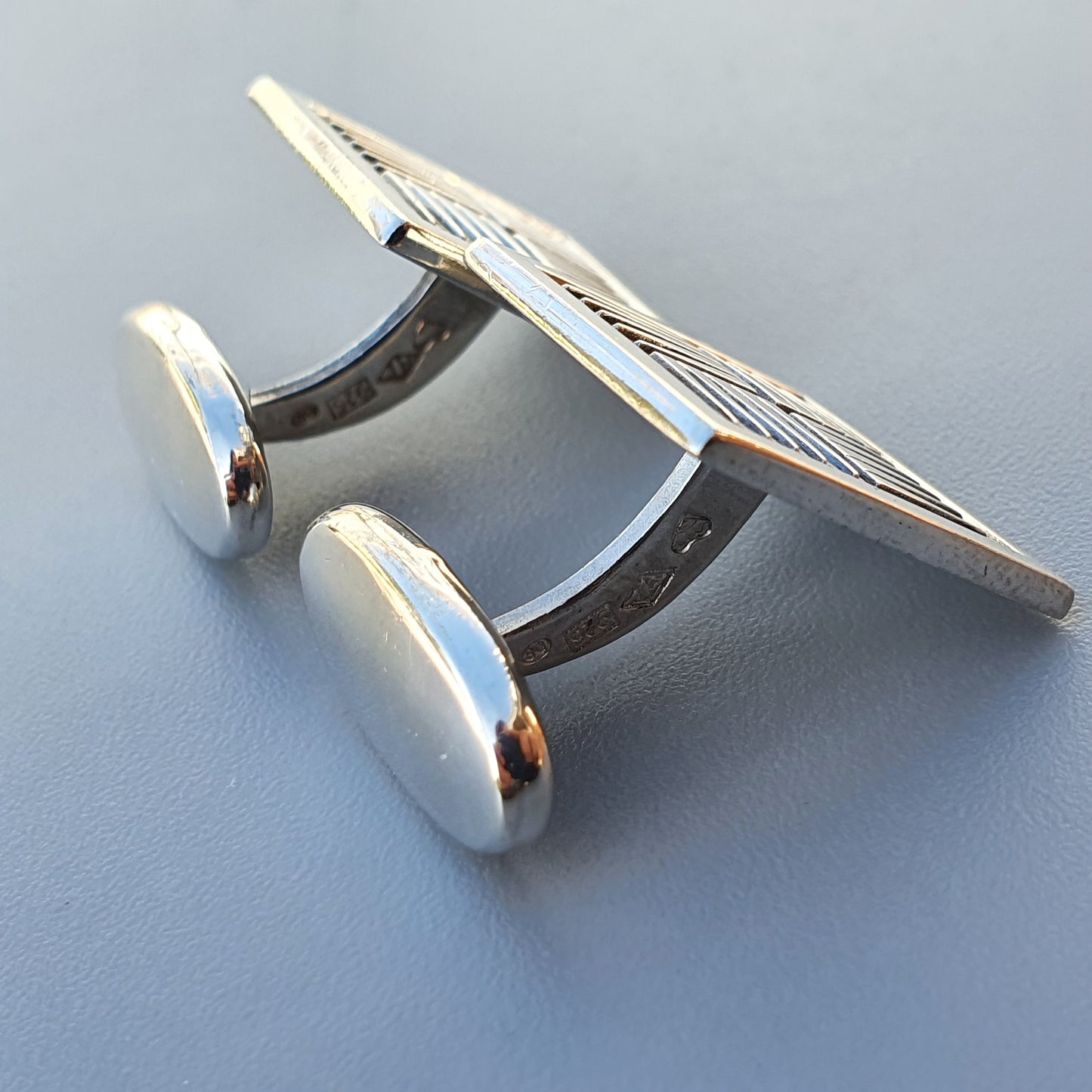 Silver cufflink with an engraved or textured square face and cylindrical posts.