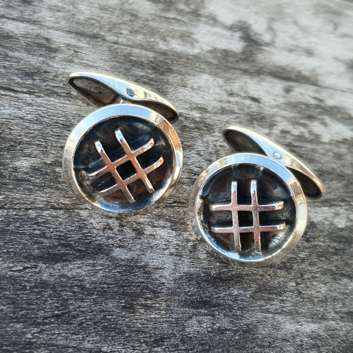 Pair of circular silver cufflinks with a cross-hatch design in the center.