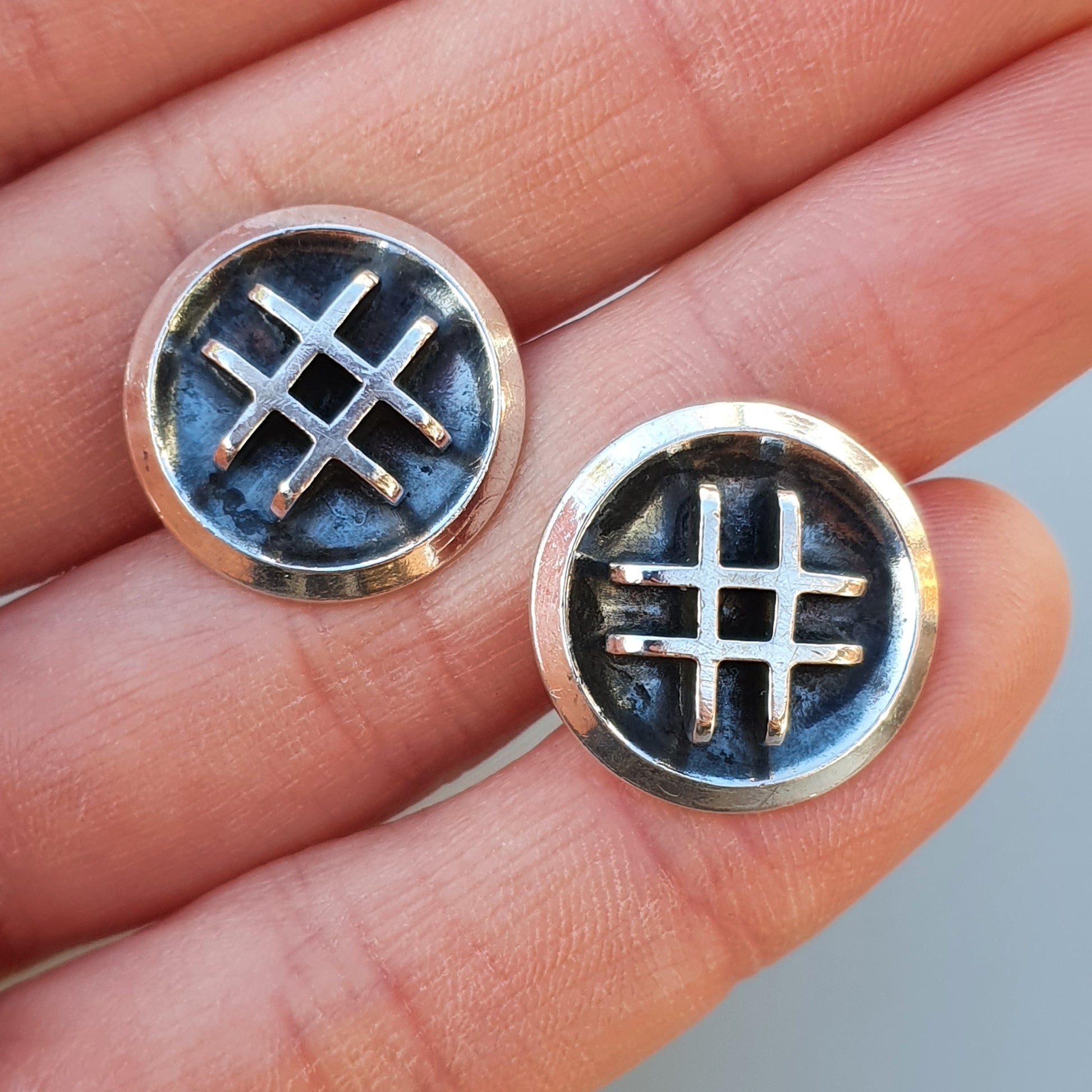 Pair of circular earrings or studs featuring a hashtag symbol design on a dark blue background.