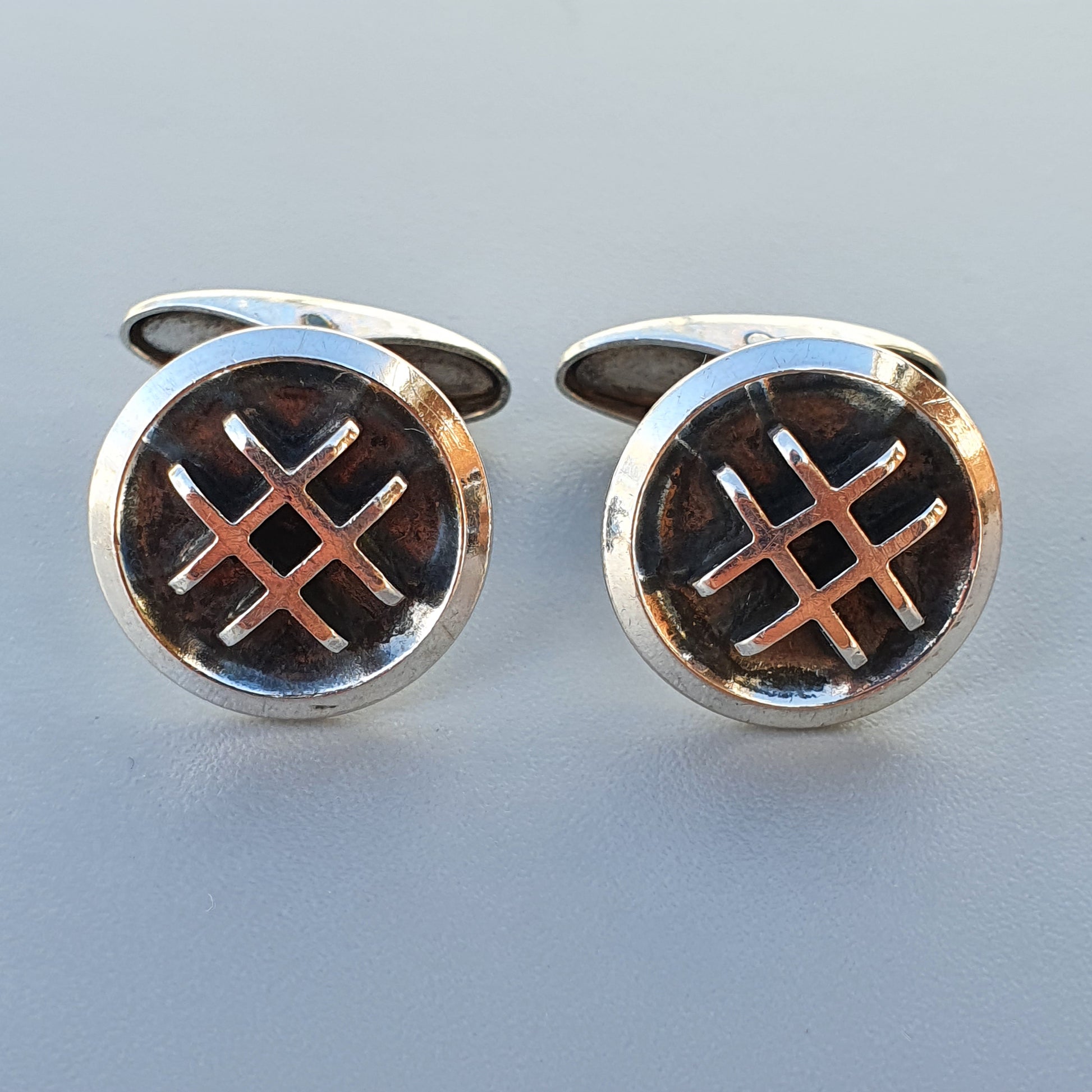 Pair of circular silver cufflinks with a crisscross pattern design.