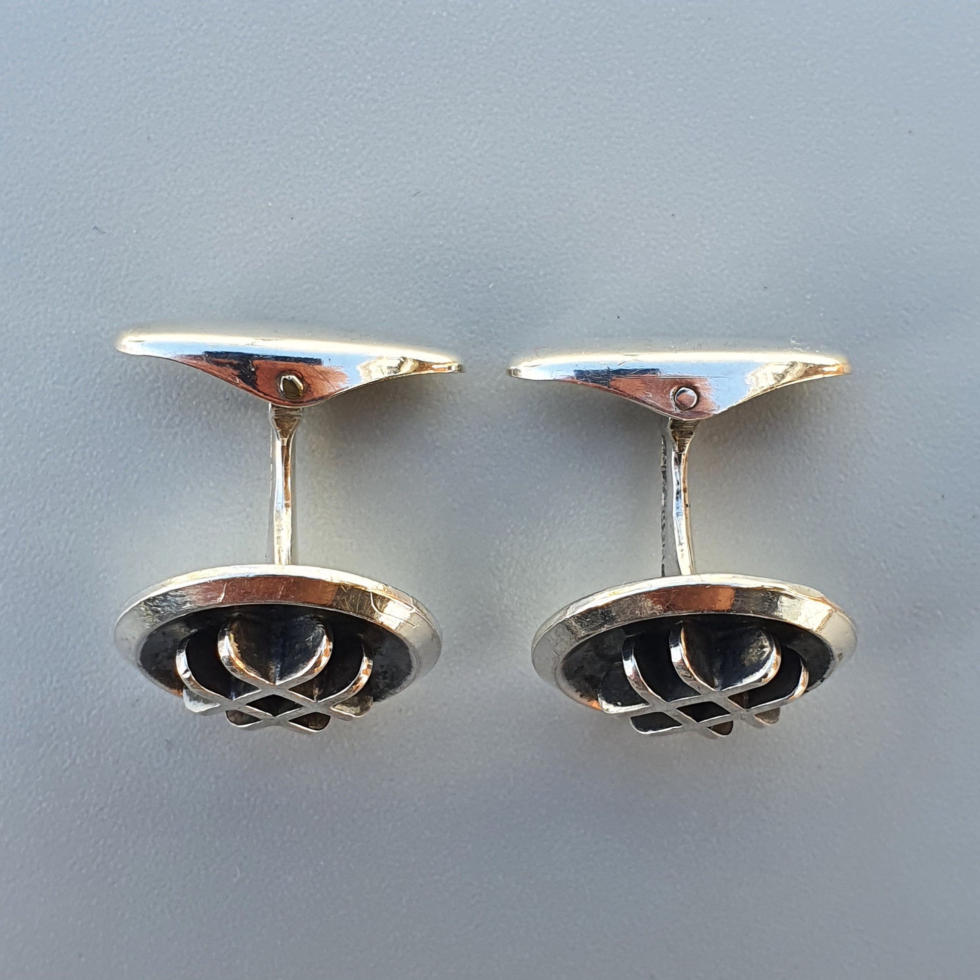 Pair of silver cufflinks with circular designs featuring interwoven patterns.