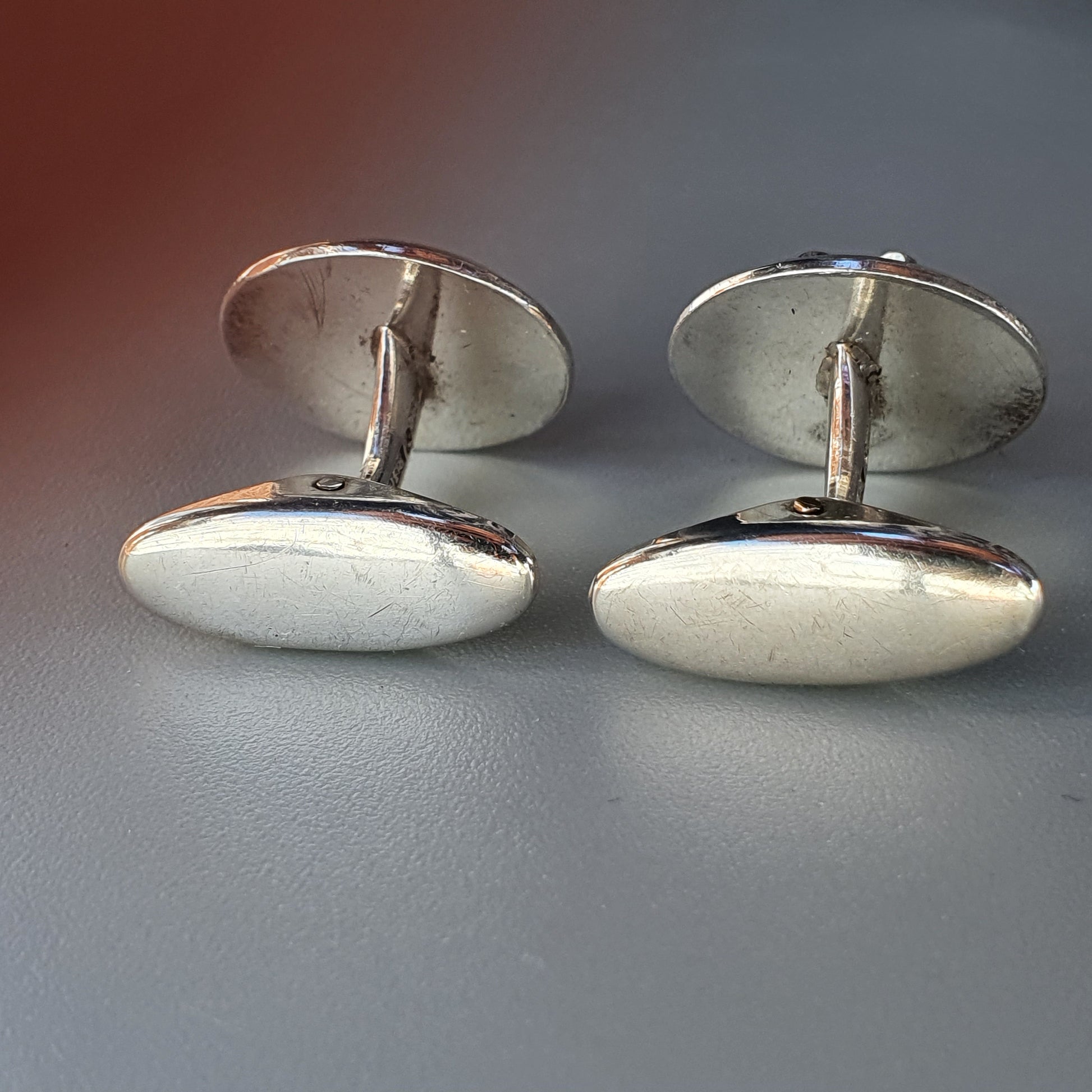 Pair of oval silver cufflinks with smooth surfaces and connecting bars.