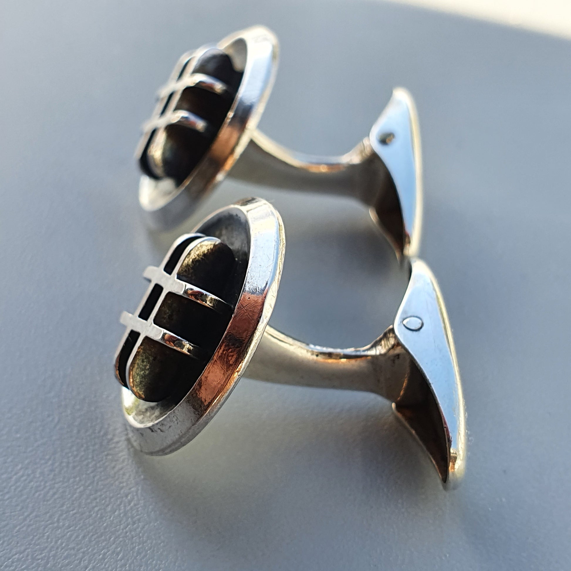 Pair of silver cufflinks with black oval centers featuring metallic lines.