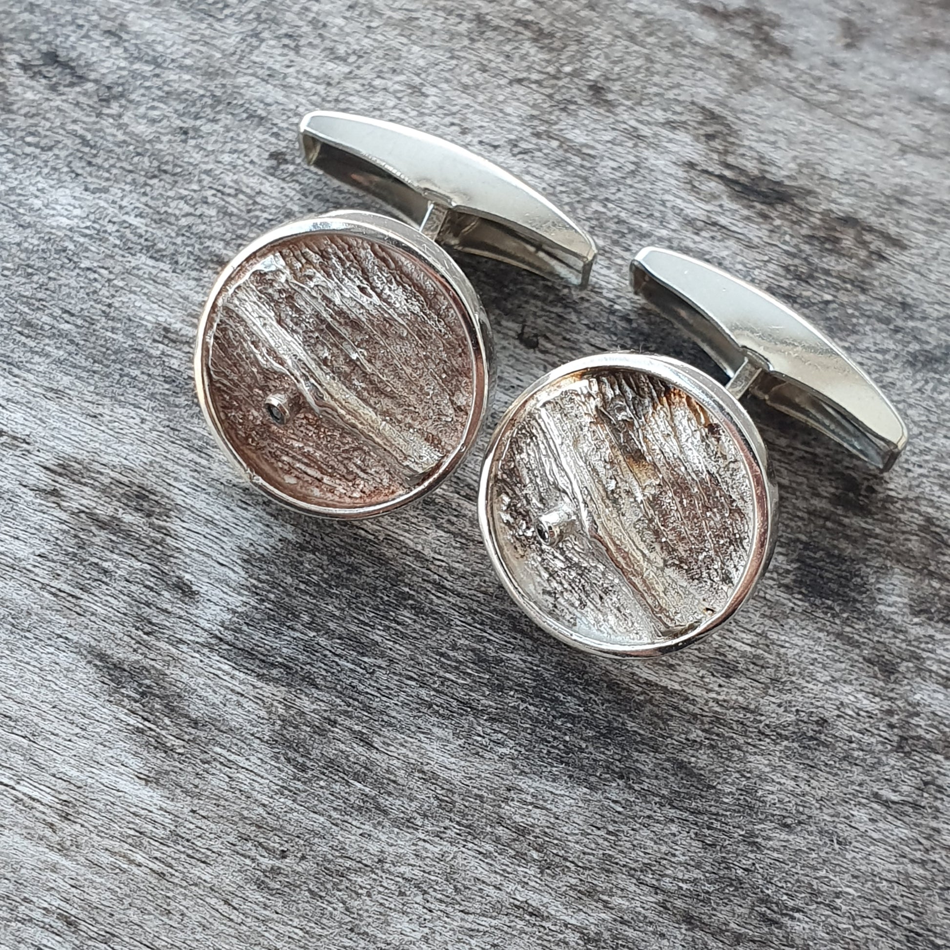 Pair of circular silver cufflinks with textured, wood-like inlays.