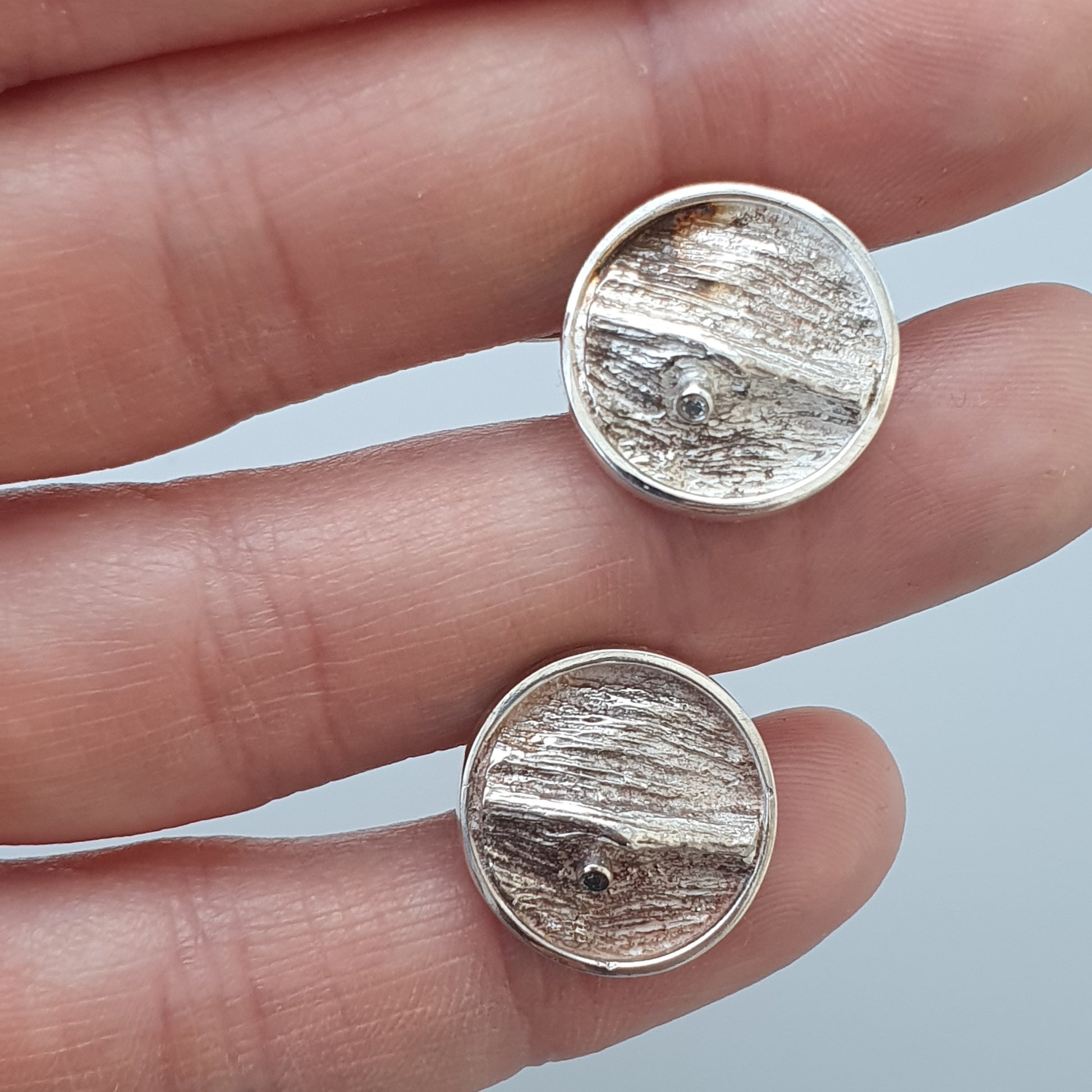 Pair of circular silver earrings with a textured, wood-grain-like pattern.