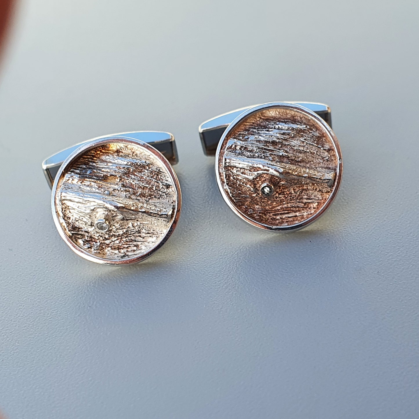 Pair of circular cufflinks featuring textured, wood-like patterns encased in silver-toned metal settings.