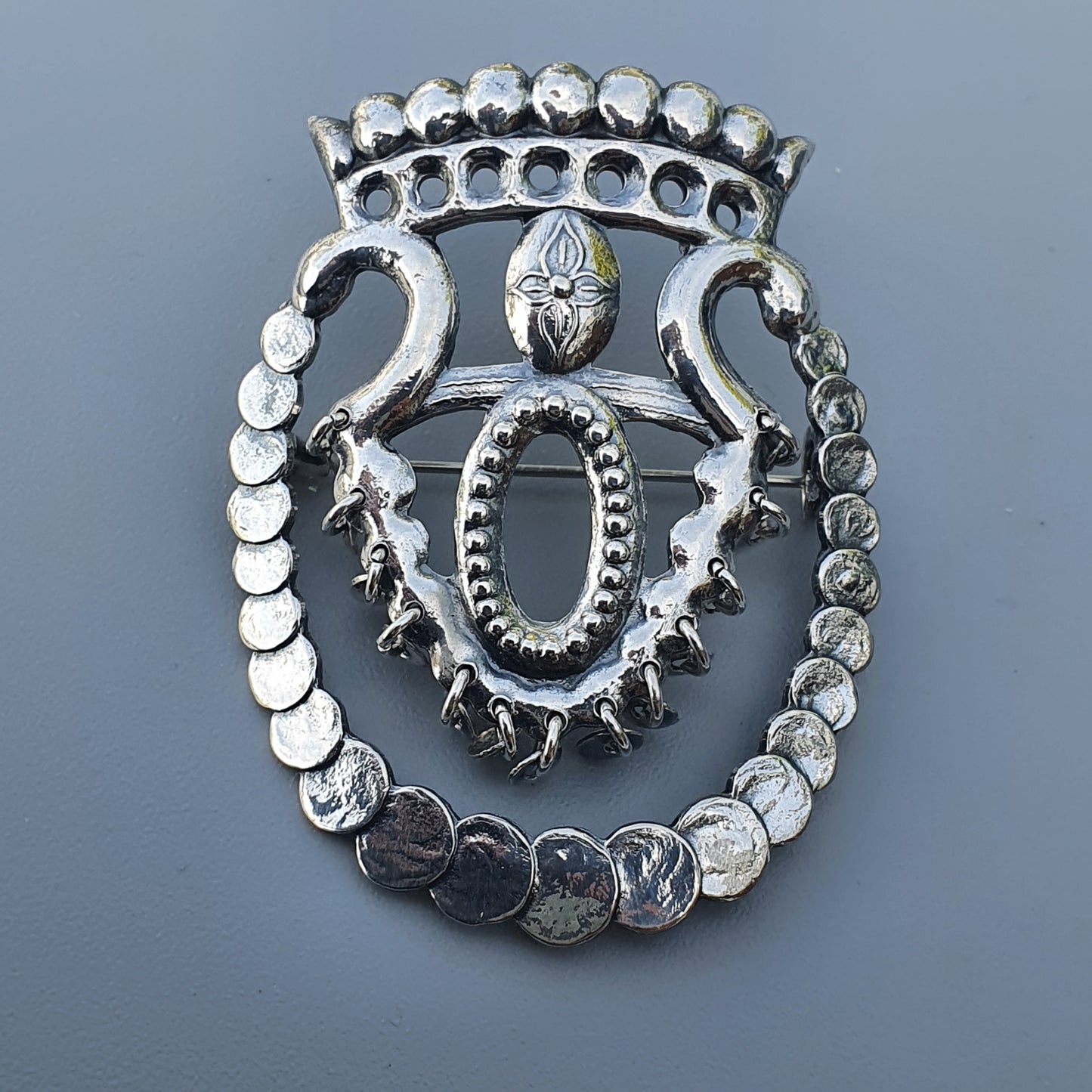 Ornate silver brooch or pendant with a crown-like design and central oval shape.