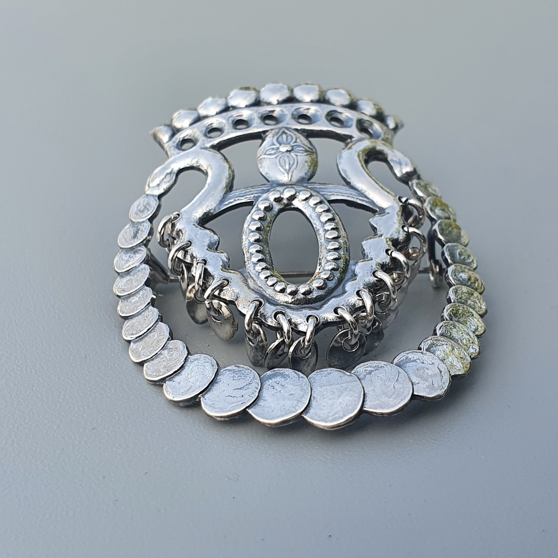 Ornate silver brooch or pendant with intricate designs and coin-like elements.