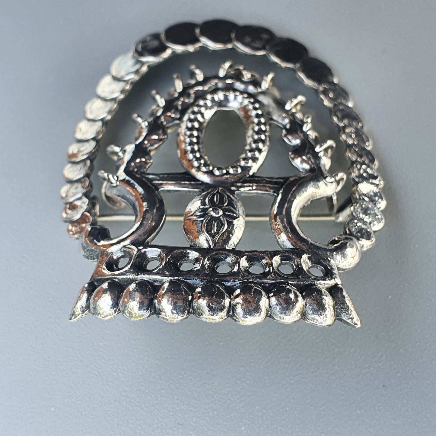 Ornate silver brooch or pendant with an intricate circular design featuring small beads and floral motifs.