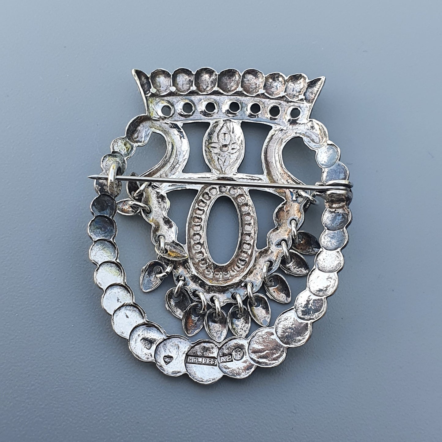 Ornate silver brooch or pin featuring a crown, horseshoe shape, and decorative elements.