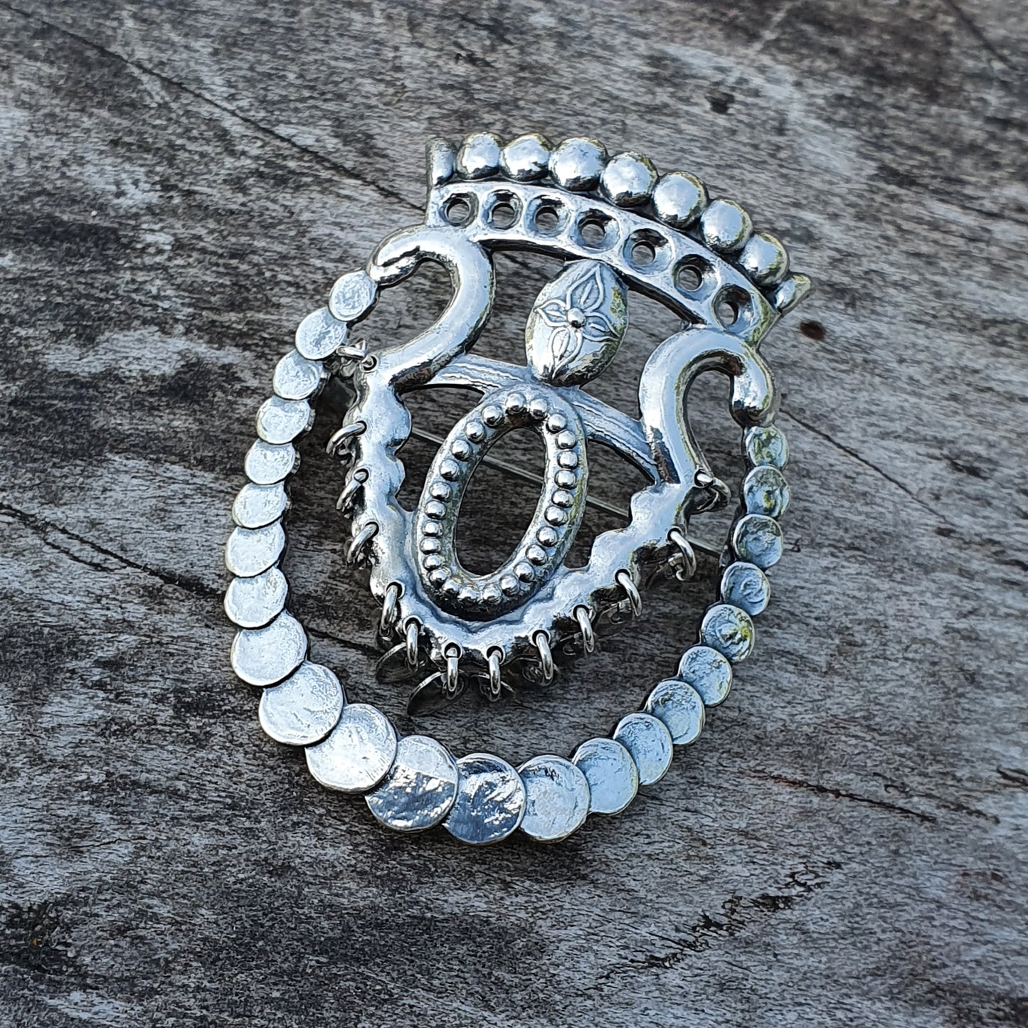 Ornate silver brooch or pendant with spiral and beaded designs.