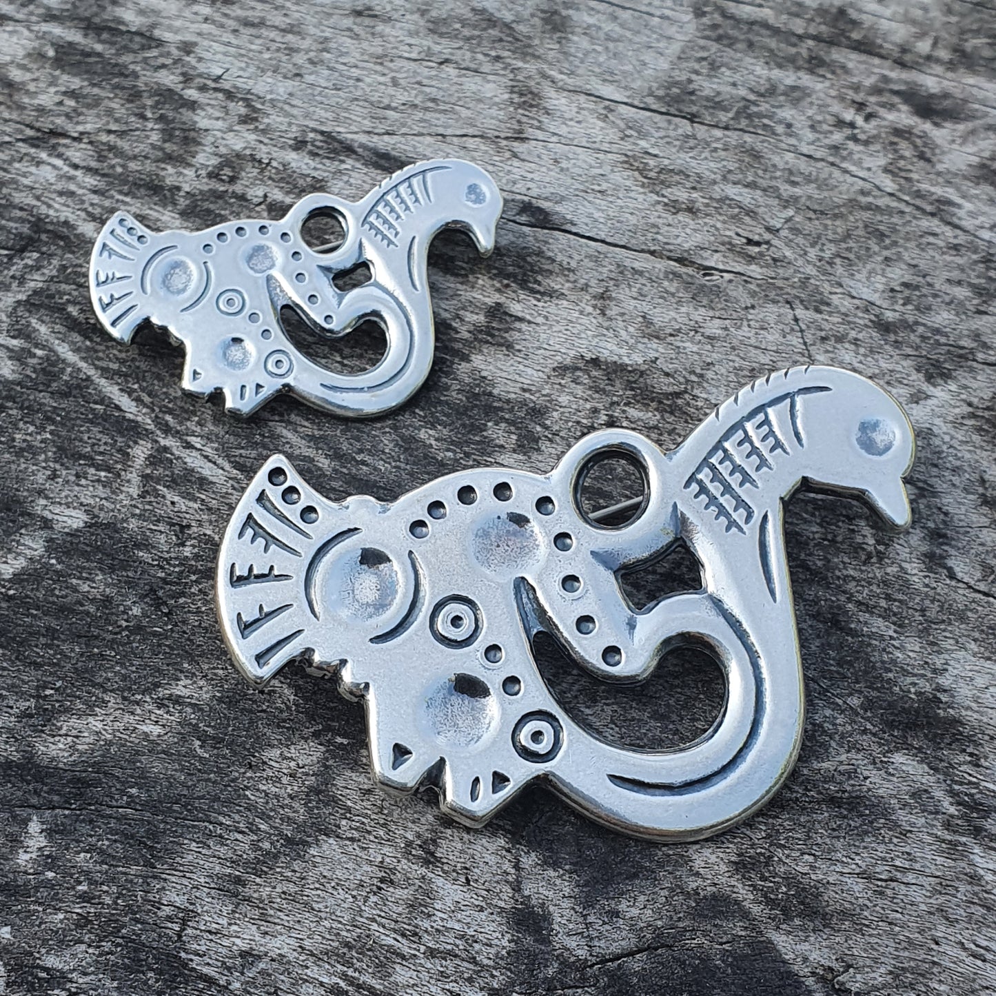 Stylized metal pendants or charms shaped like fantastical creatures with curved bodies and bird-like features.