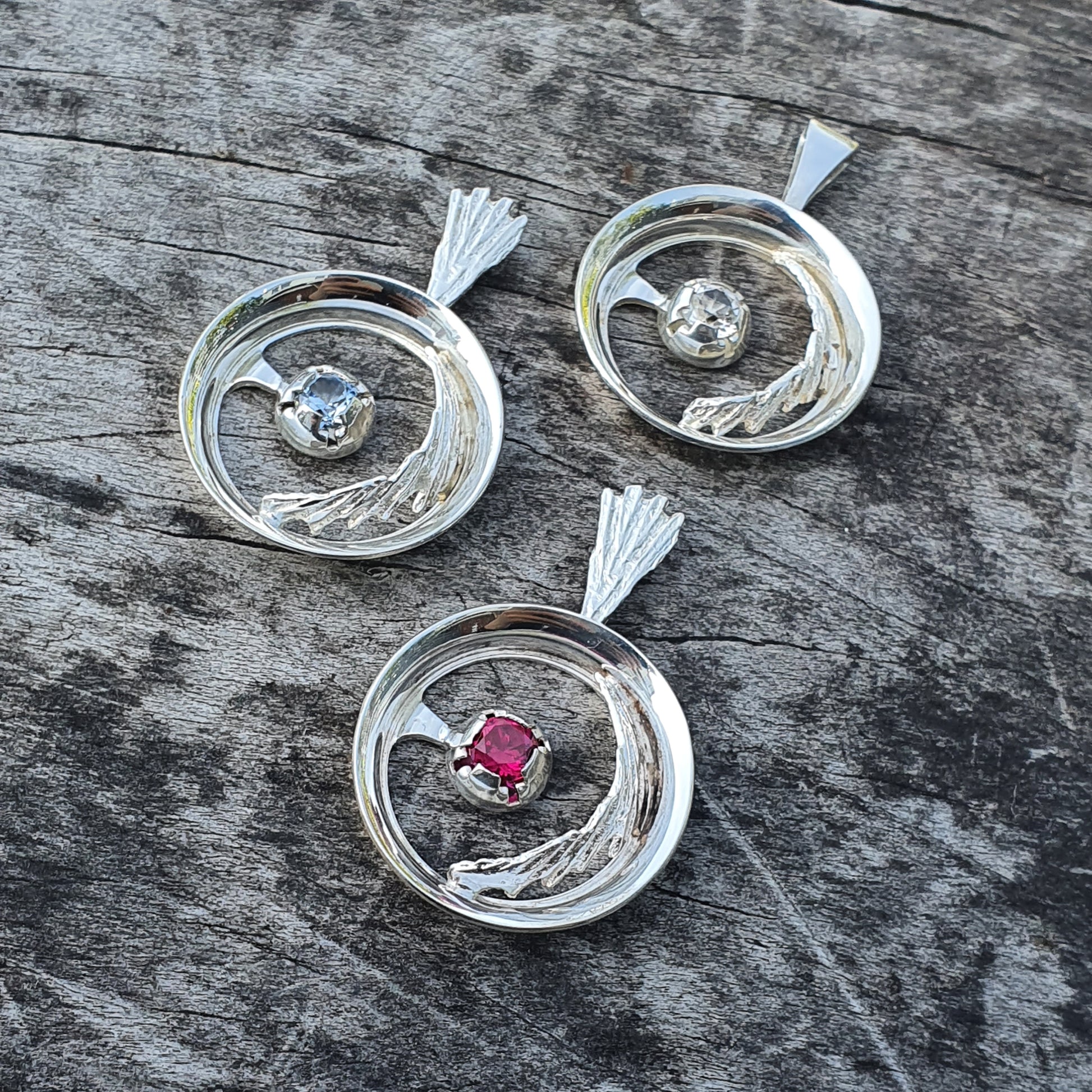 Silver circular pendants with gemstones set in swirling designs.