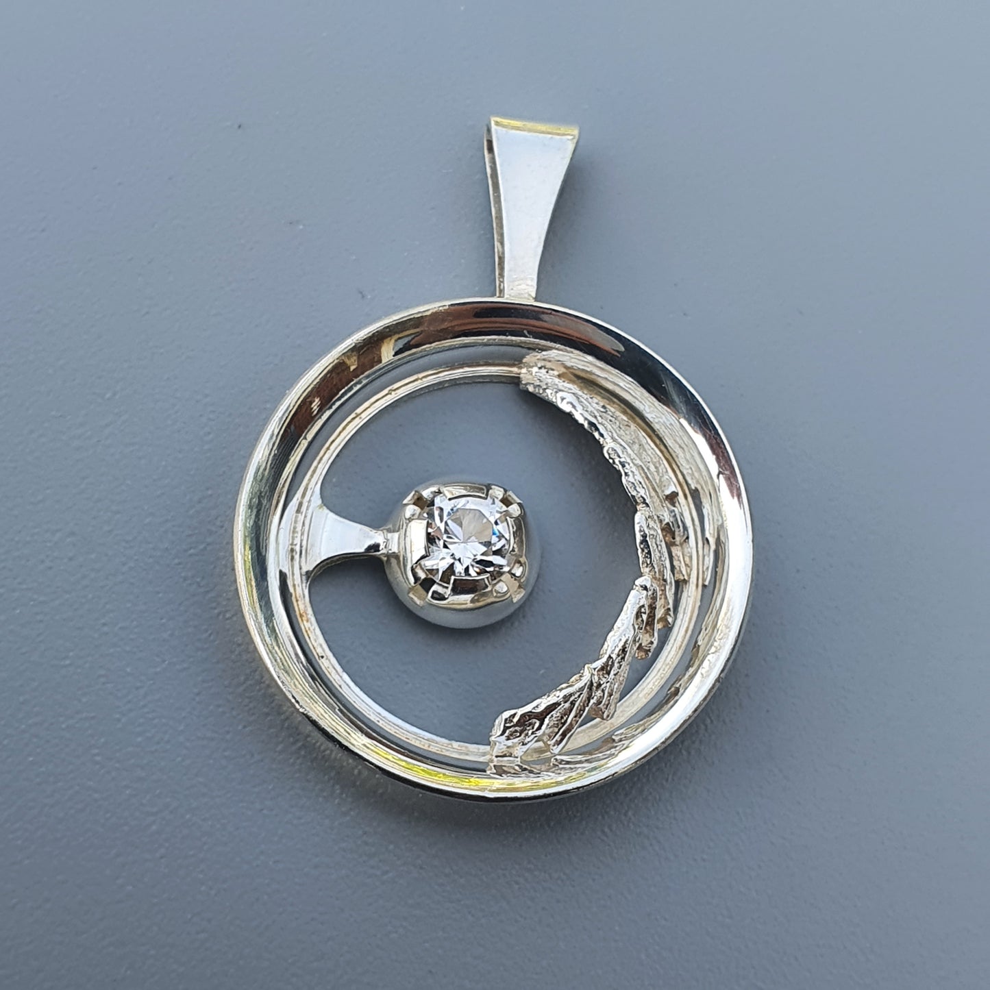 Circular silver pendant with a diamond-like stone set within a crescent shape.