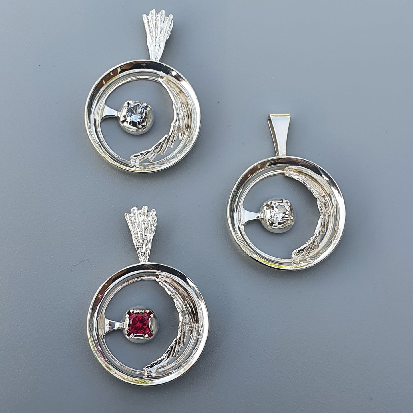 Circular silver pendants with gemstones set in swirling designs.