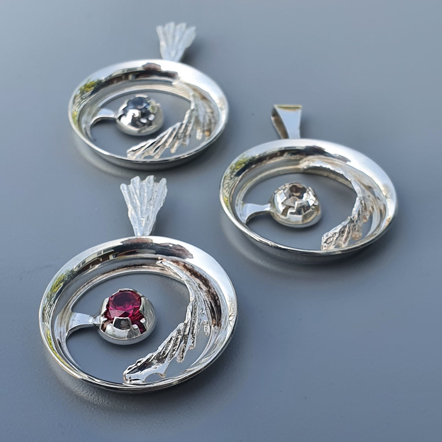 Silver pendants with circular designs featuring gemstones and leaf-like accents.