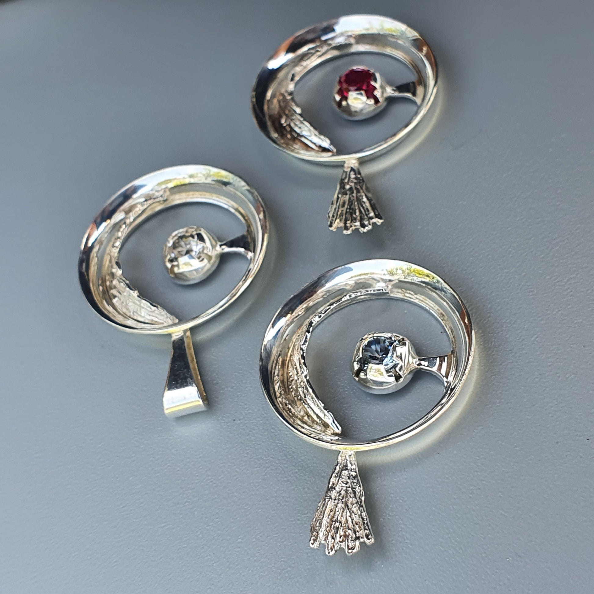 Silver jewelry pieces featuring circular designs with gemstones and decorative pendants.