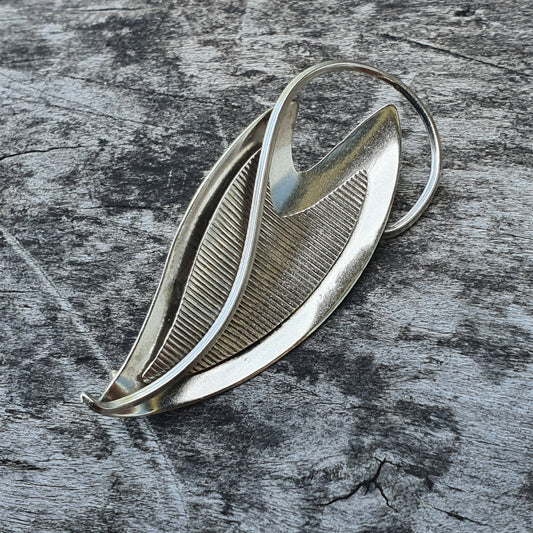 Leaf-shaped silver brooch with curved, overlapping metallic elements.