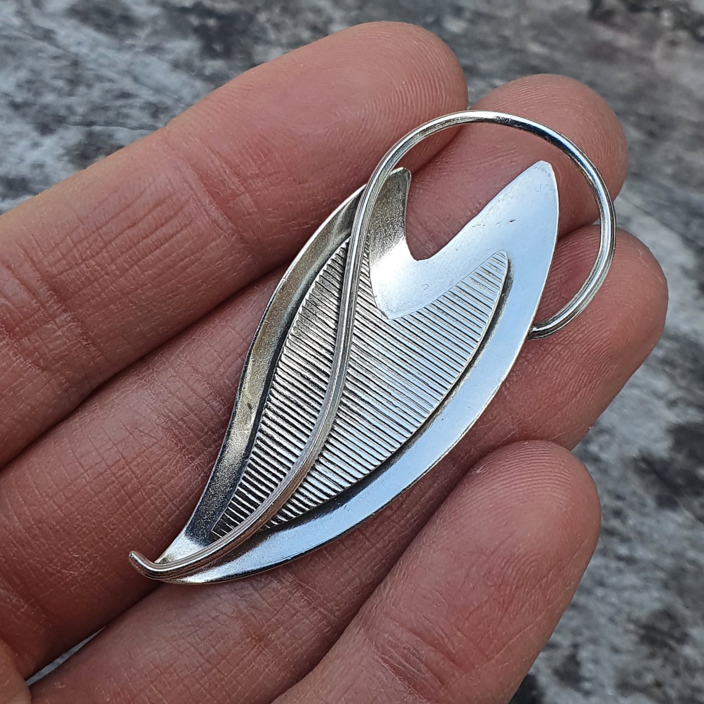 Silver leaf-shaped brooch or pendant with textured detailing.