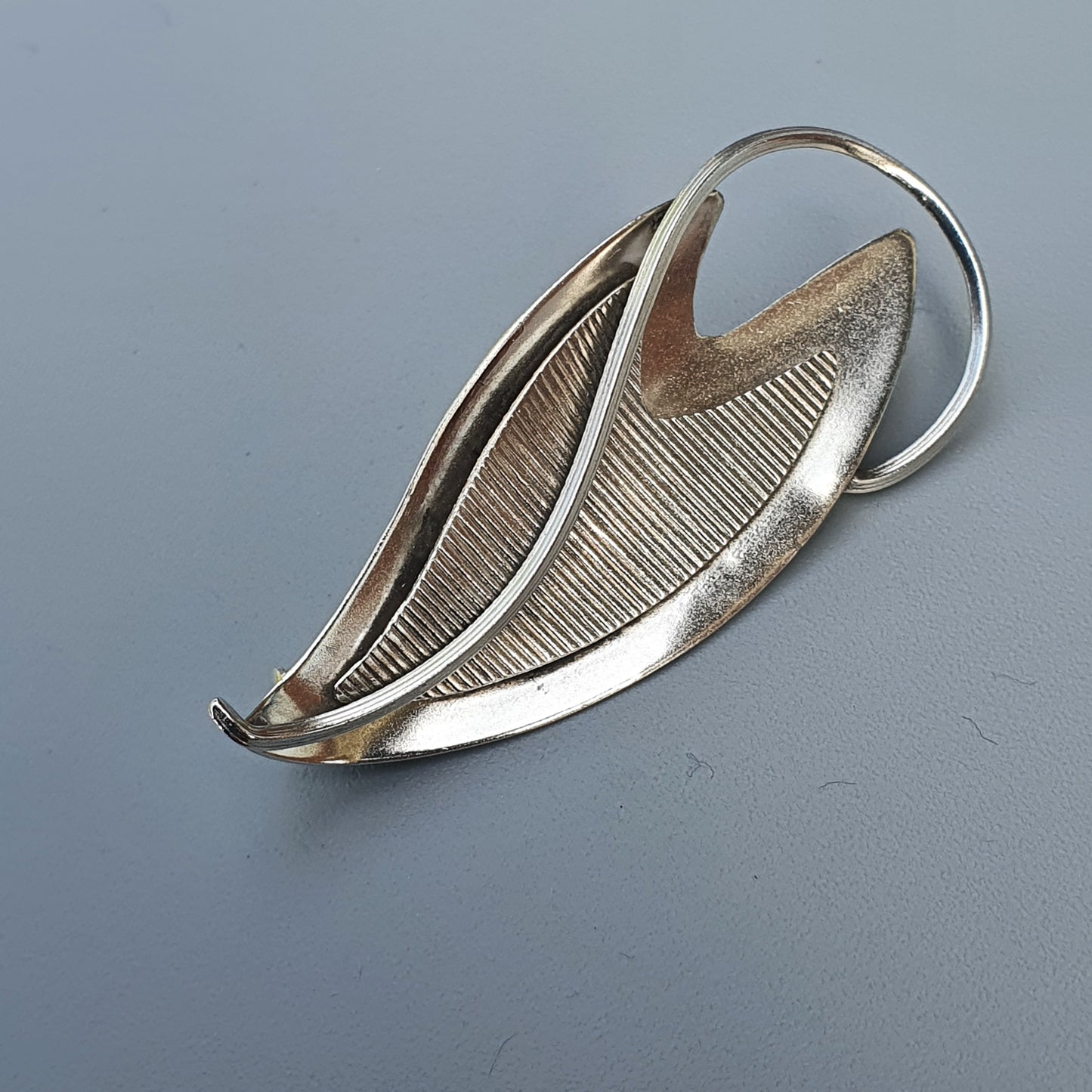 Leaf-shaped silver brooch with a textured surface and curved lines.