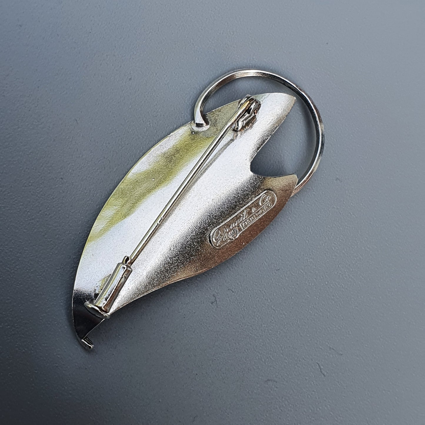 Silver-colored teardrop-shaped fishing lure with a hook and metal ring attached.